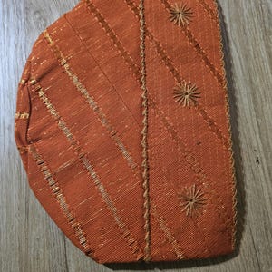 May include: A brown fabric hat with gold stitching and embroidered flower designs.