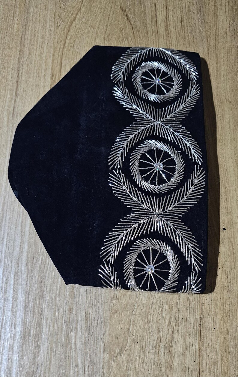 May include: A black velvet hat with silver embroidery. The embroidery features three circular designs with a central rhinestone.