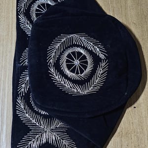 May include: A black velvet fabric with silver embroidery in a circular pattern. The fabric is folded in half and has a decorative design.