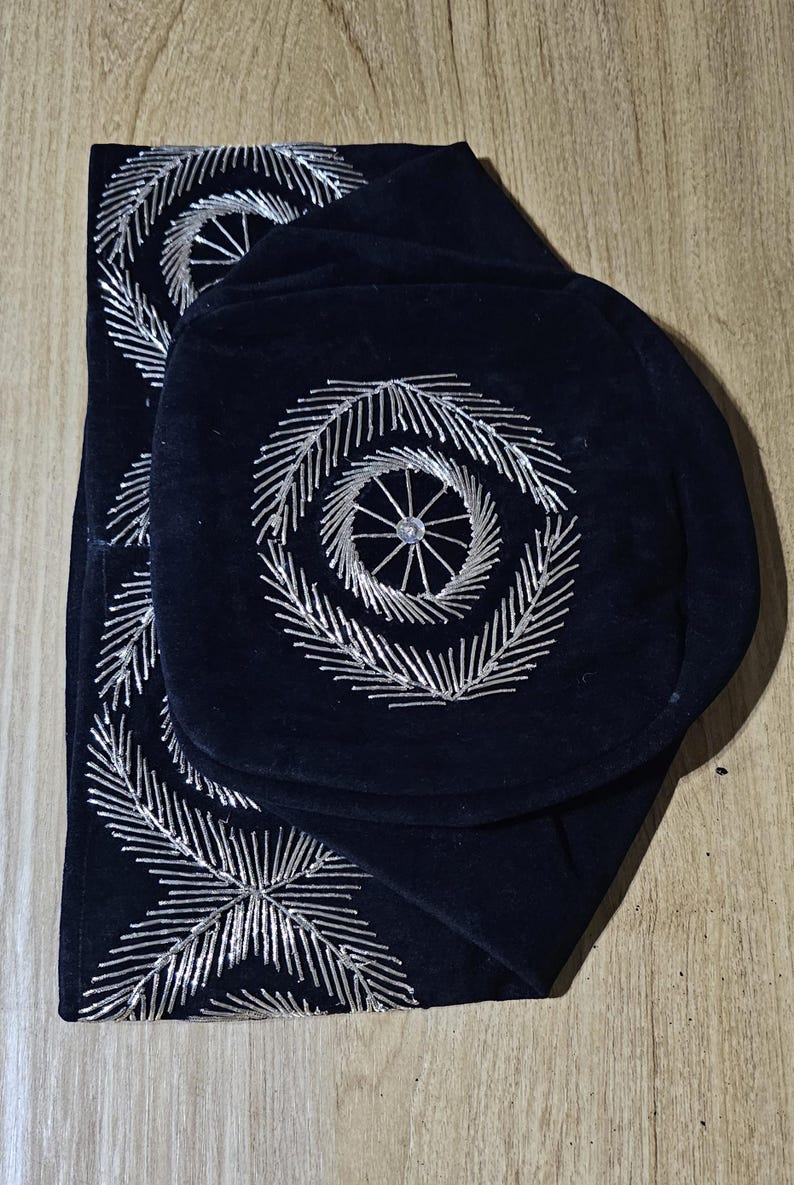May include: A black velvet fabric with silver embroidery in a circular pattern. The fabric is folded in half and has a decorative design.