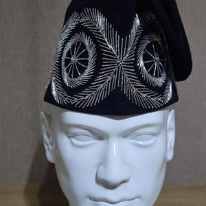 May include: A black velvet hat with silver embroidery. The embroidery features a circular design with a star in the center.