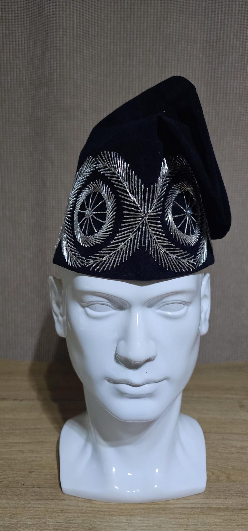 May include: A black velvet hat with silver embroidery. The embroidery features a circular design with a star in the center.