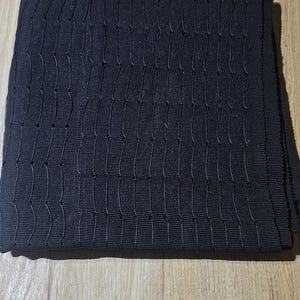 Può includere: Un tessuto piegato, blu navy scuro, con un motivo strutturato e tessuto. Il tessuto è di forma rettangolare, con linee verticali e orizzontali che creano un design a griglia. Il materiale è probabilmente un tessuto.