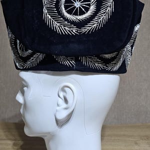 May include: A black velvet hat with silver embroidery. The embroidery features a circular design with a central star.