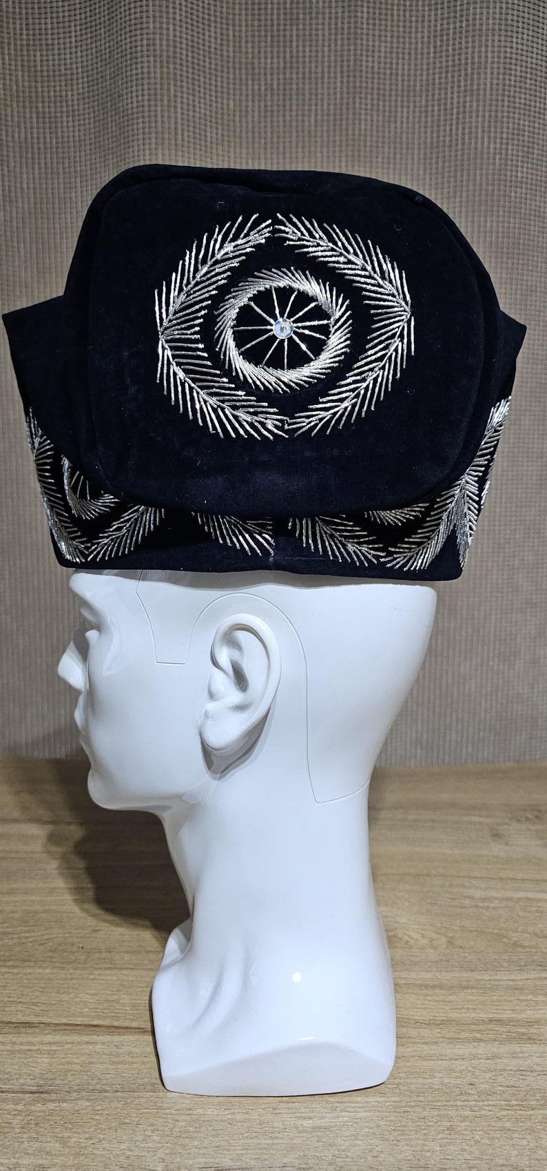 May include: A black velvet hat with silver embroidery. The embroidery features a circular design with a central star.