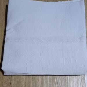Può includere: Un tessuto blu chiaro piegato con una trama a coste. Il tessuto è piegato con cura, mettendo in risalto la trama e il colore. L'articolo sembra essere un capo d'abbigliamento o un tessuto.