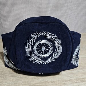 May include: A dark blue hat with a circular design embroidered in silver thread. The design features a central circle with radiating lines.