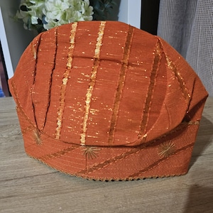 May include: A brown and gold patterned hat with a scalloped edge. The hat is made of a woven fabric with a shiny gold thread running through it.