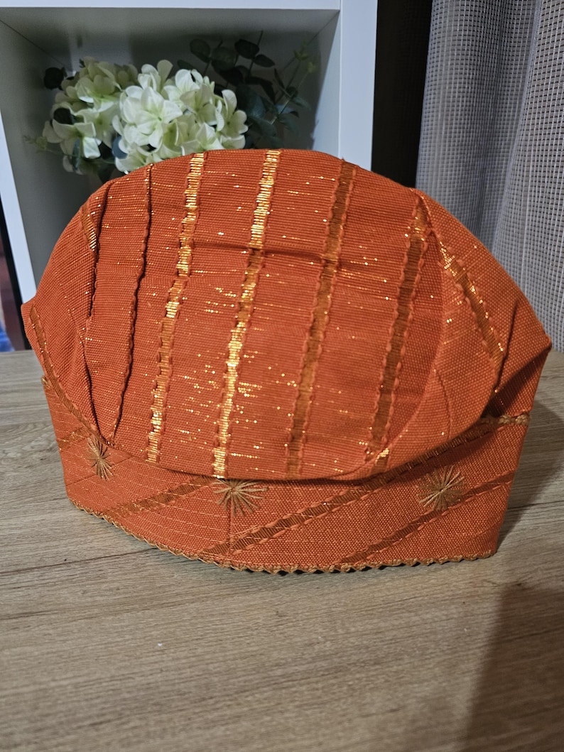 May include: A brown and gold patterned hat with a scalloped edge. The hat is made of a woven fabric with a shiny gold thread running through it.
