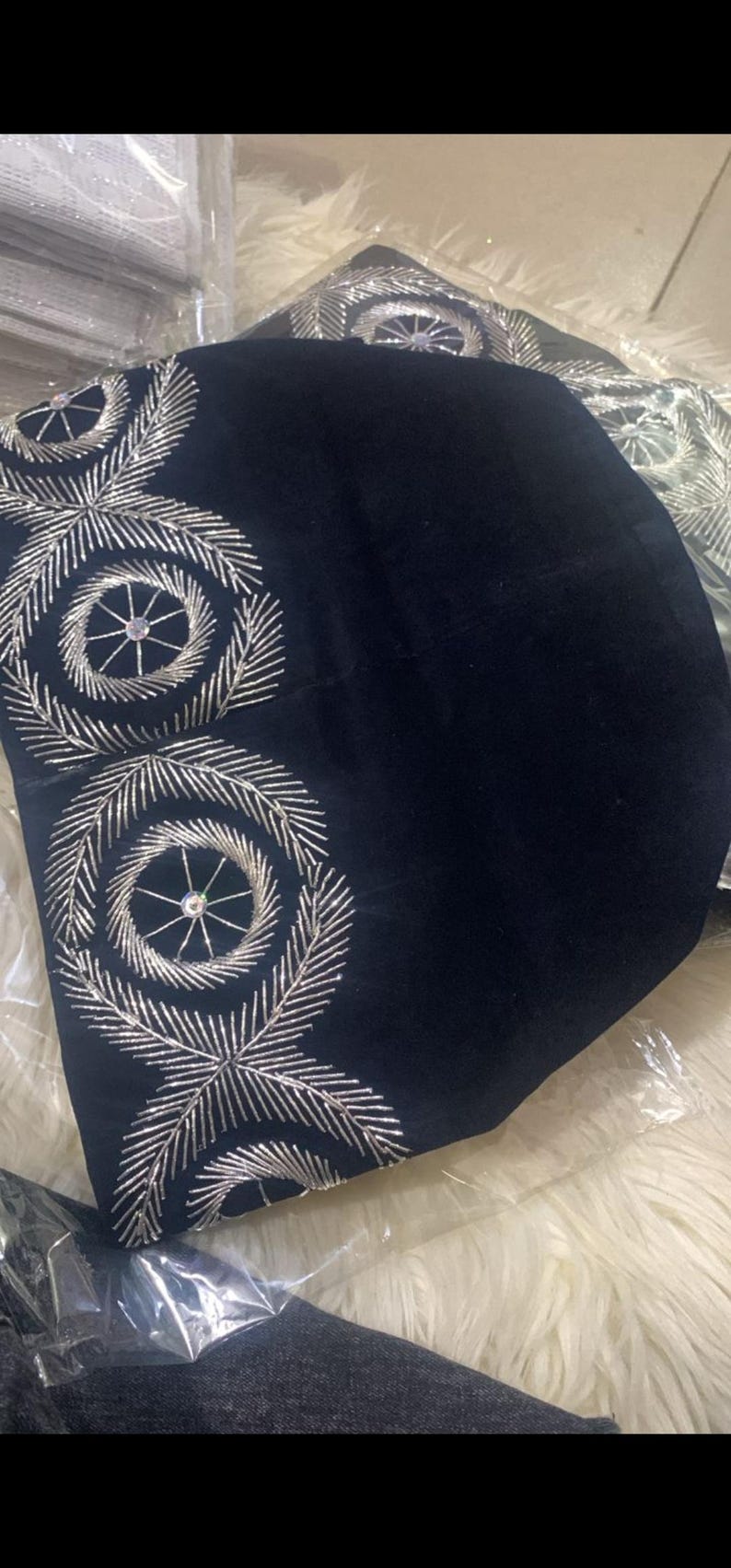 May include: A black velvet hat with silver embroidery. The embroidery features a circular design with a small rhinestone in the center.