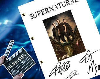 May include: A white script page with the title "SUPERNATURAL" printed in black. The page features a photo of three men standing on a rocky cliff. The page is signed by three people, with the names "Jared", "Jensen", and "Misha" written in black ink.