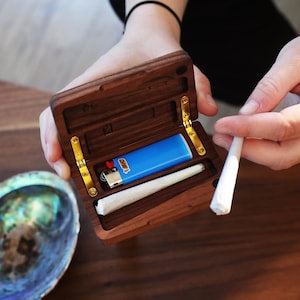 May include: A wooden box with a hinged lid, containing a blue lighter and a white rolling paper. The box is open and the lighter and rolling paper are visible.