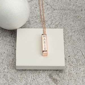 May include: A rose gold necklace with a vertical bar pendant engraved with the name "MARIE".