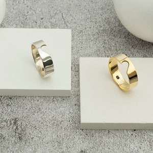 Puede incluir: Dos anillos con un corte en forma de corazón. El anillo de la izquierda es de plata y el anillo de la derecha es de oro.