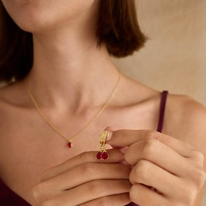 May include: Gold hoop earrings with dangling red teardrop-shaped stones.