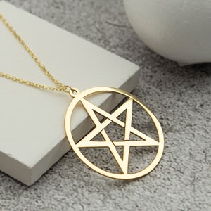 May include: A gold necklace with a large, circular pendant featuring a pentagram design. The pendant is hollow and the star is outlined in gold.