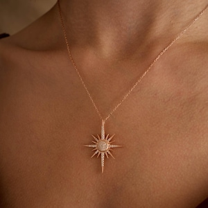 May include: A rose gold necklace featuring a starburst pendant set with clear cubic zirconia stones.