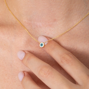 May include: A gold chain necklace with a small blue and white evil eye charm.