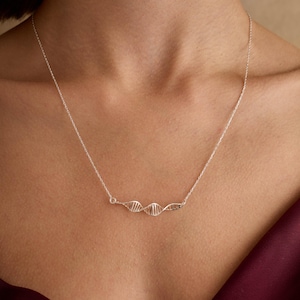 Puede incluir: Un collar de plata con una cadena delicada y un colgante de hélice de ADN tridimensional.