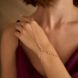 May include: A rose gold chain bracelet with a delicate star design. The bracelet is adjustable and can be worn on the wrist or as a hand chain.