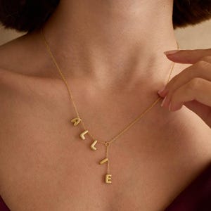 May include: A gold necklace with a dangling charm that spells out the name "ALLIE".