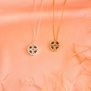 May include: Two delicate necklaces with four-leaf clover pendants. The pendants are adorned with sparkling clear stones and green gemstones. One necklace has a silver chain, and the other has a gold chain.