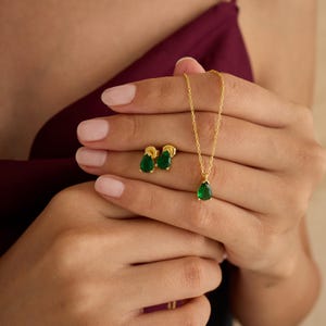 以下が含まれることがあります： 雫型の緑色の宝石が付いた金のネックレスとイヤリングのセットです。