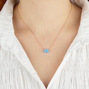 May include: A delicate gold chain necklace with a small blue elephant pendant. The elephant is made of a sparkly material, possibly opal or turquoise.