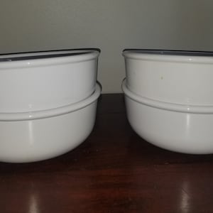 May include: Two white ceramic soup bowls with handles. The bowls are stacked, with a handle on each side. The bowls have a simple, clean design, and are likely for serving soup or other dishes.