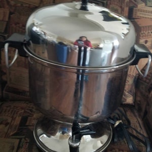 May include: A silver, electric coffee percolator with a shiny, reflective surface. The percolator has a black handle and a black knob on the top.