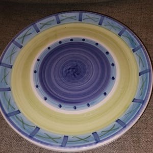 May include: A large, round ceramic plate with a blue, yellow, and green design. The plate has a concentric circle pattern with a blue center and yellow outer ring.