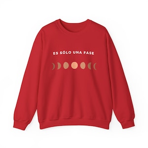 May include: Red sweatshirt with the text "ES SÓLO UNA FASE" in white and a row of moon phases in gold.