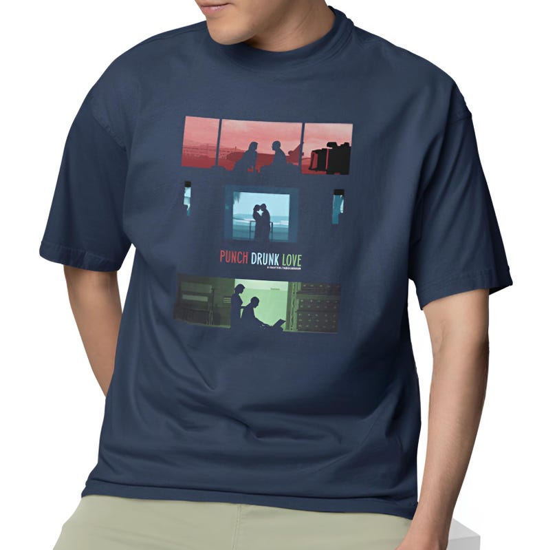 May include: Navy blue t-shirt featuring a graphic design with three rectangular panels. The panels depict silhouettes of people in various scenes, with the text "PUNCH DRUNK LOVE" below the middle panel. The shirt is a short-sleeved crew neck.