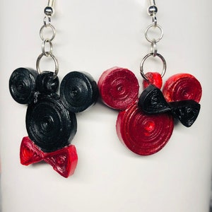May include: A pair of black and red Mickey Mouse and Minnie Mouse earrings. The earrings are made of paper and have a bow tie on the bottom.