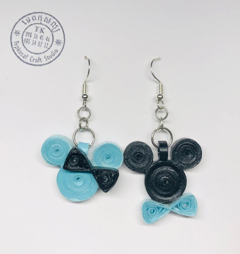 May include: A pair of blue and black paper quilled earrings shaped like Mickey Mouse. The earrings are on a silver hook.