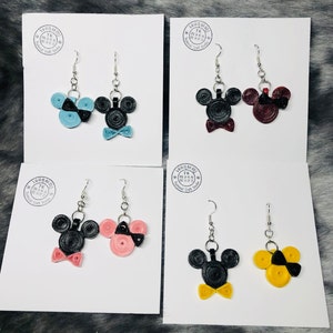 May include: Four pairs of handmade Mickey Mouse and Minnie Mouse earrings. Each pair features a black Mickey Mouse head with a bow tie and a Minnie Mouse head with a bow. The bows are in different colors: blue, red, pink, and yellow.