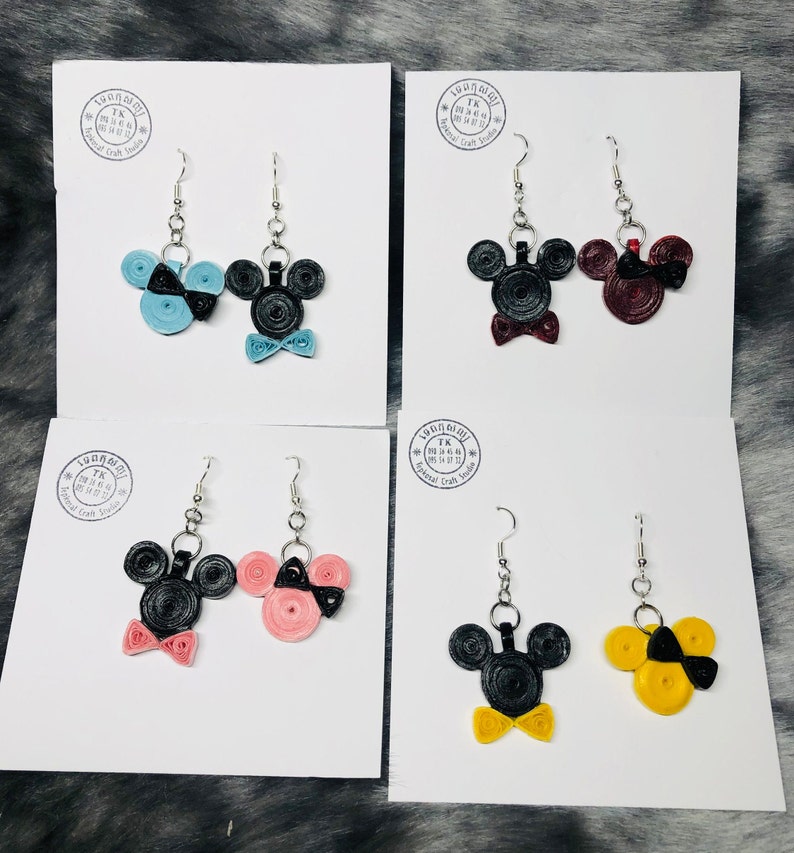 May include: Four pairs of handmade Mickey Mouse and Minnie Mouse earrings. Each pair features a black Mickey Mouse head with a bow tie and a Minnie Mouse head with a bow. The bows are in different colors: blue, red, pink, and yellow.