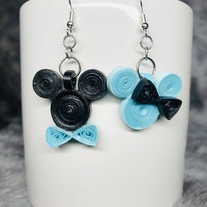May include: A pair of dangle earrings featuring a black and blue paper quilling design. One earring is shaped like Mickey Mouse with a blue bow tie, and the other earring is a blue swirl with a black bow tie.