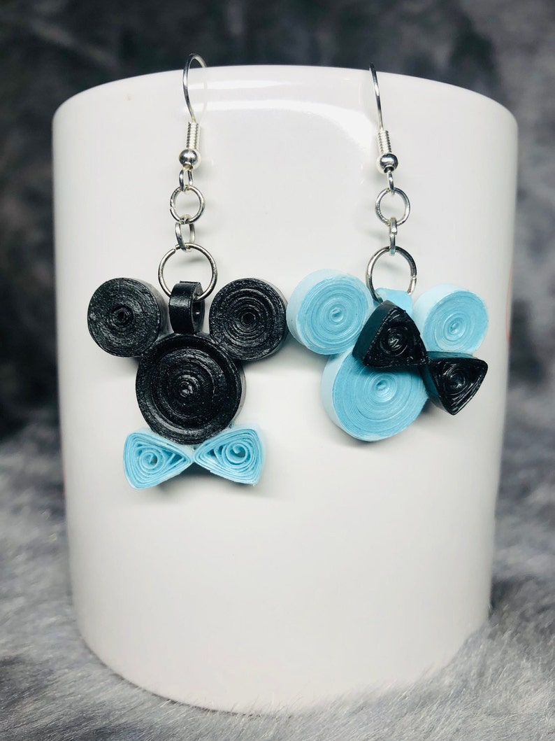 May include: A pair of dangle earrings featuring a black and blue paper quilling design. One earring is shaped like Mickey Mouse with a blue bow tie, and the other earring is a blue swirl with a black bow tie.