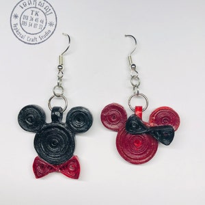 May include: A pair of black and red Mickey Mouse and Minnie Mouse earrings. The earrings are made of paper and are shaped like the characters' heads. The earrings are hanging from silver hooks.