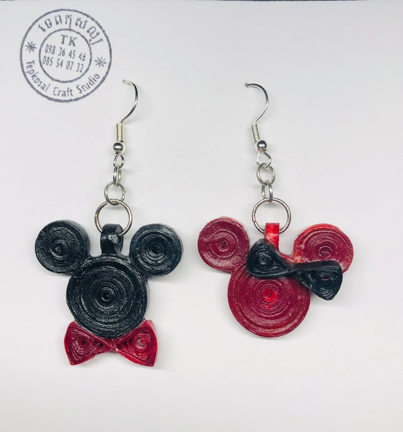 May include: A pair of black and red Mickey Mouse and Minnie Mouse earrings. The earrings are made of paper and are shaped like the characters' heads. The earrings are hanging from silver hooks.