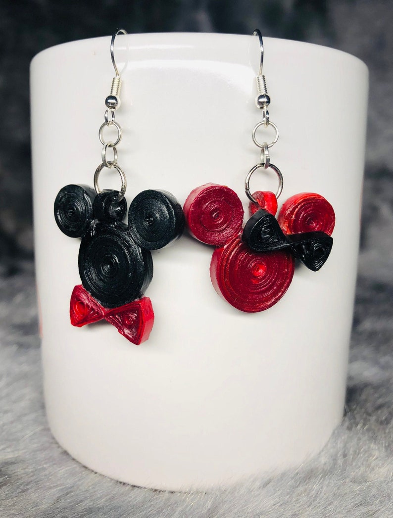 May include: A pair of black and red Mickey Mouse and Minnie Mouse earrings. The earrings are made of paper and have a bow tie on the bottom.