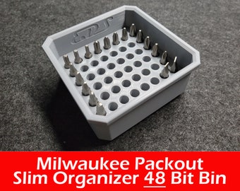 May include: A gray plastic storage bin with 48 compartments for holding small items, such as screwdriver bits. The bin is labeled "Milwaukee Packout Slim Organizer 48 Bit Bin".