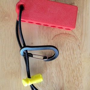 May include: A red plastic bit holder with a black elastic strap and a carabiner clip. The holder has multiple slots for bits and a yellow plastic clip on the strap.