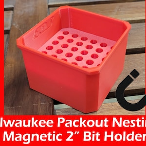 May include: Red plastic 2" bit holder with a magnetic base and a grid of holes for organizing drill bits.  The holder is labeled "Packout Nestling".