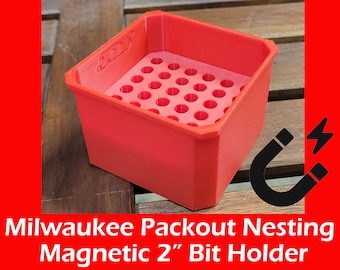 May include: Red plastic 2" bit holder with a magnetic base and a grid of holes for organizing drill bits.  The holder is labeled "Packout Nestling".