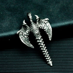 Puede incluir: Un colgante plateado con un diseño de dragón detallado con las alas extendidas. La cola del dragón está enroscada en un punto y el colgante está diseñado para ser usado como collar.