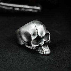 Op de afbeelding: Een zilveren schedelring met een gedetailleerd ontwerp. De ring is gemaakt van metaal en heeft een realistisch schedelontwerp.