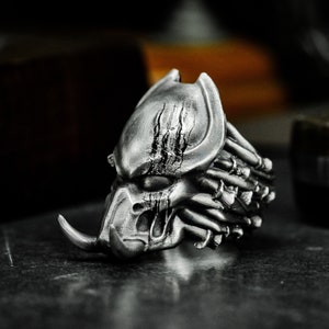 Könnte beinhalten: Ein silberner Predator-Maskenring mit detaillierter Skulptur und einer strukturierten Oberfläche.