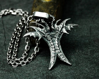 Puede incluir: Un collar de cadena de plata con un colgante tridimensional detallado en forma de criatura con garras y una superficie texturizada.